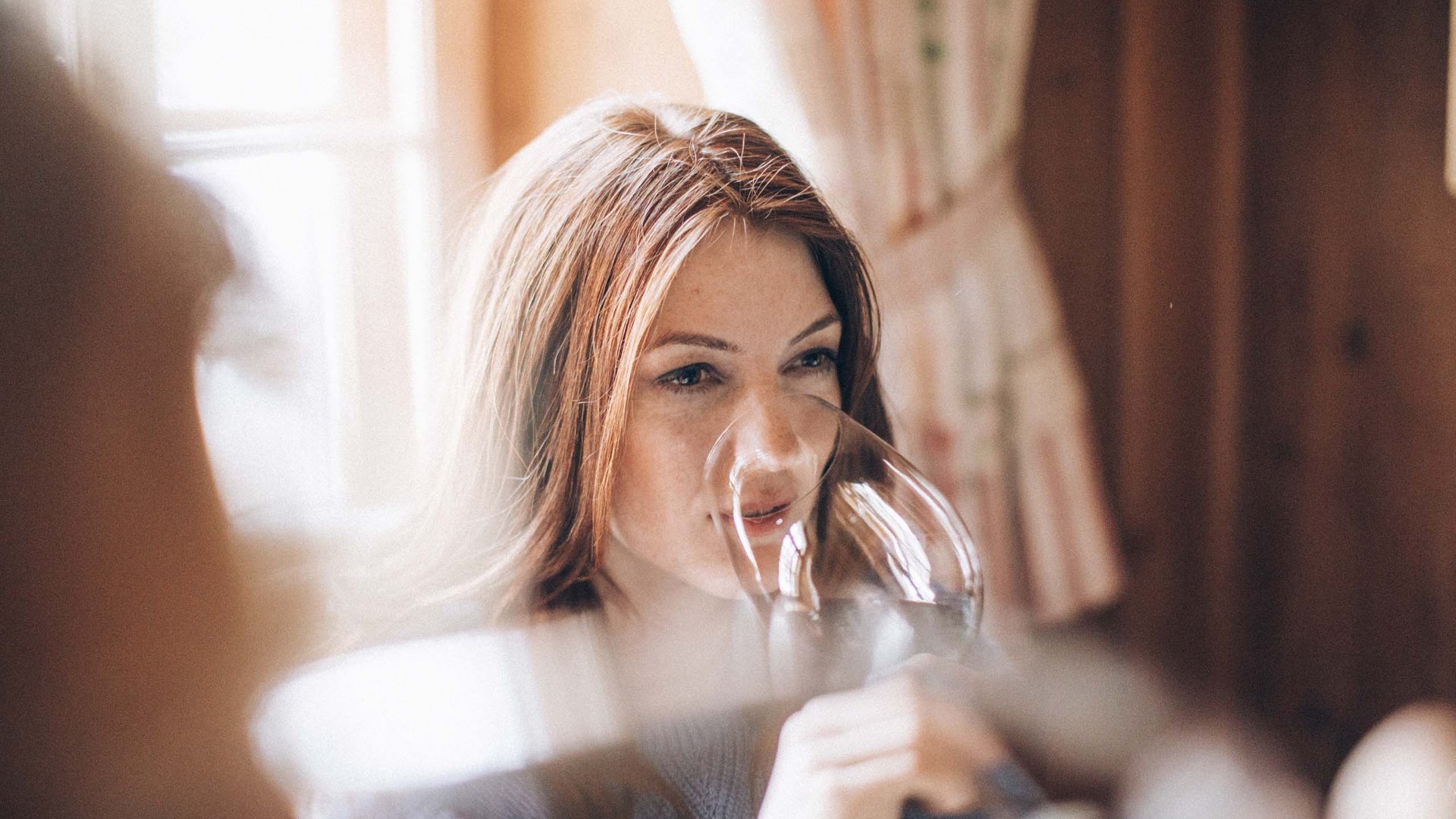 Woman smelling wine in a glass by a window with soft light